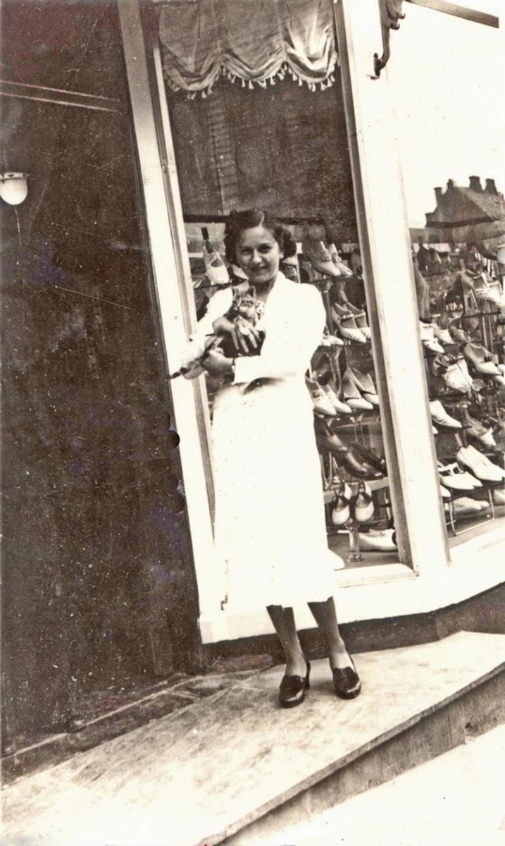 Edith Rabinowitz foran M. Rabinowitz forretning i Strandgt. 165. Utstillingsvindu med sko i bakgrunnen.