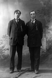 Studioportrett i helfigur av to menn.