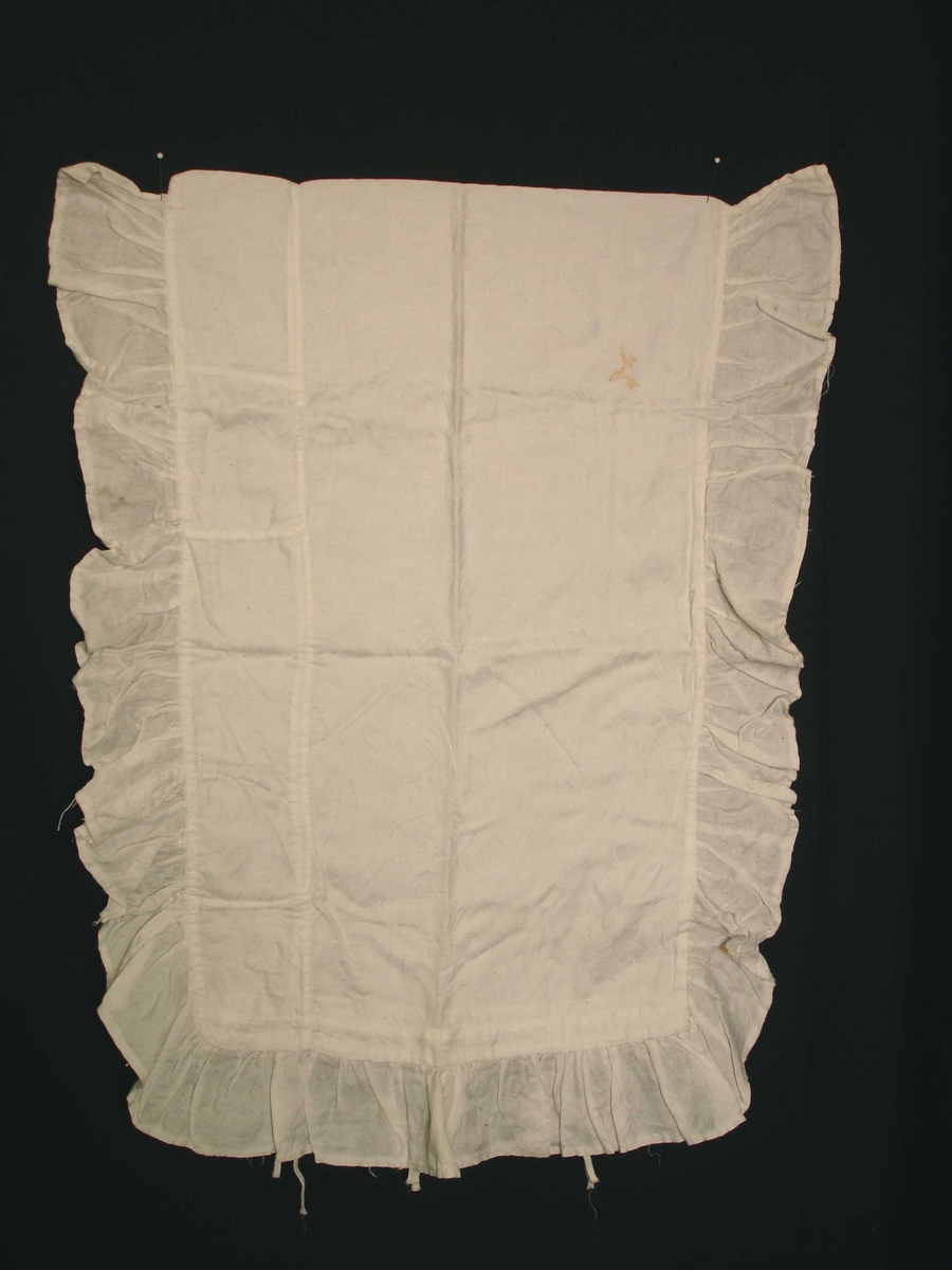 Dynetrekk til dukkeseng, hvit med 7 cm kappe på tre kanter. i bomullsstoff med innvevde blomstermotiver. Laget i slutten av 1800 og begynnelsen av 1900. 
