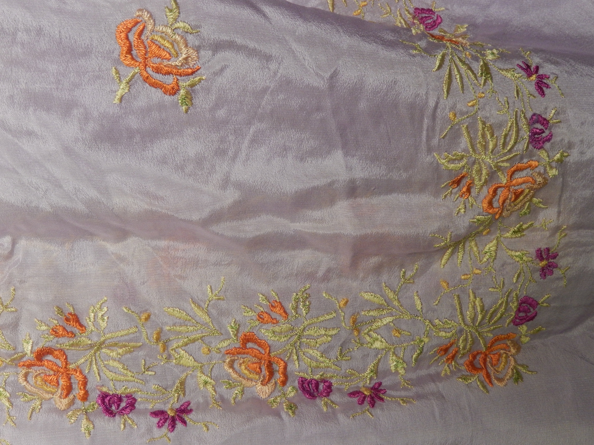 Sjal i silke med frynser.  20 cm lange frynser. Lilla firkantet sjal med broderier, blomstermotiv i fargene gult, orange og mørk lilla. 