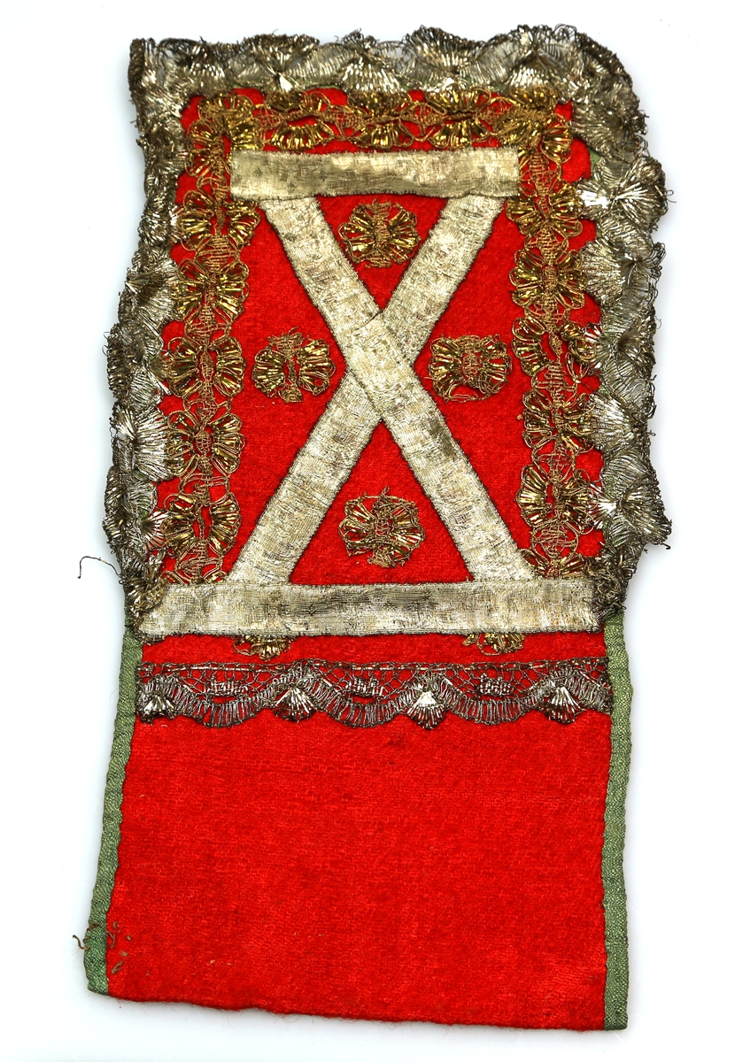 Bringeduk av rødt, grovt ulltøy kantet med grønt bånd av blank tråd og pyntet med metallkniplinger og metallbånd