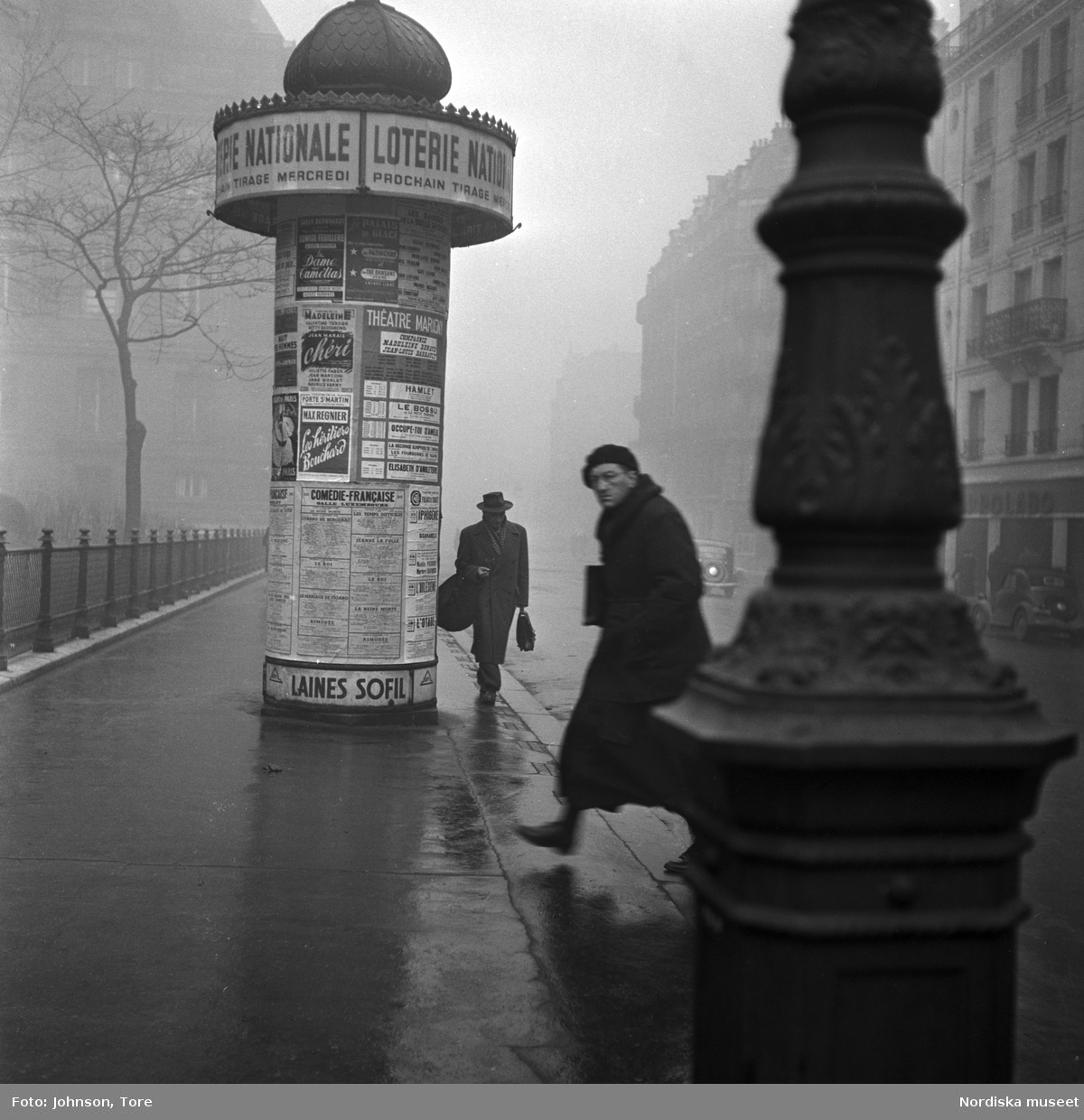 Fotgängare på en gata i Paris, annonspelare i bakgrunden.