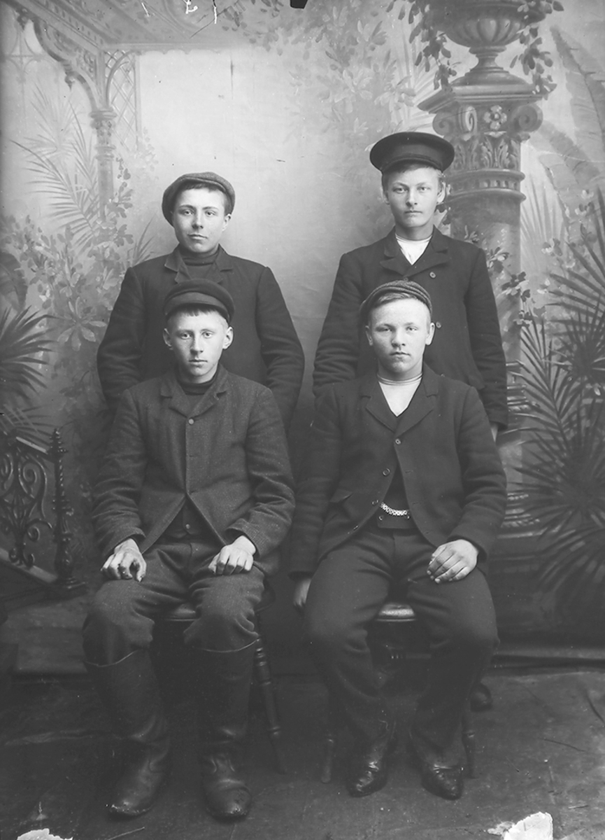 Portrett. 4 menn ca. 20 år. To sitter, 2 står bak. Alle med lue. Bildet er tatt på Reine i Lofoten.