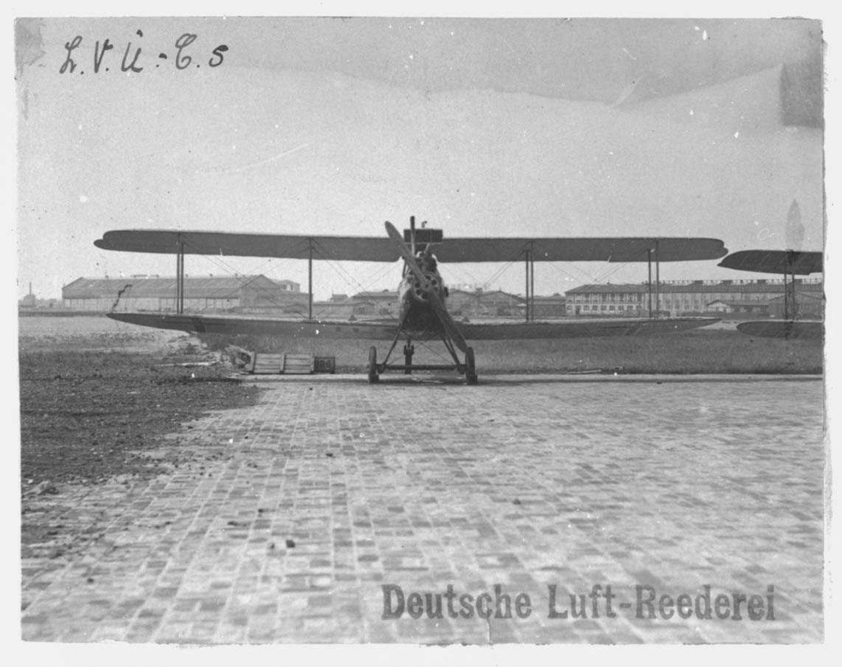 Ett fly på bakken.LVG C.V of Deutsche Luft-Reederei. Bygninger i bakgrunn