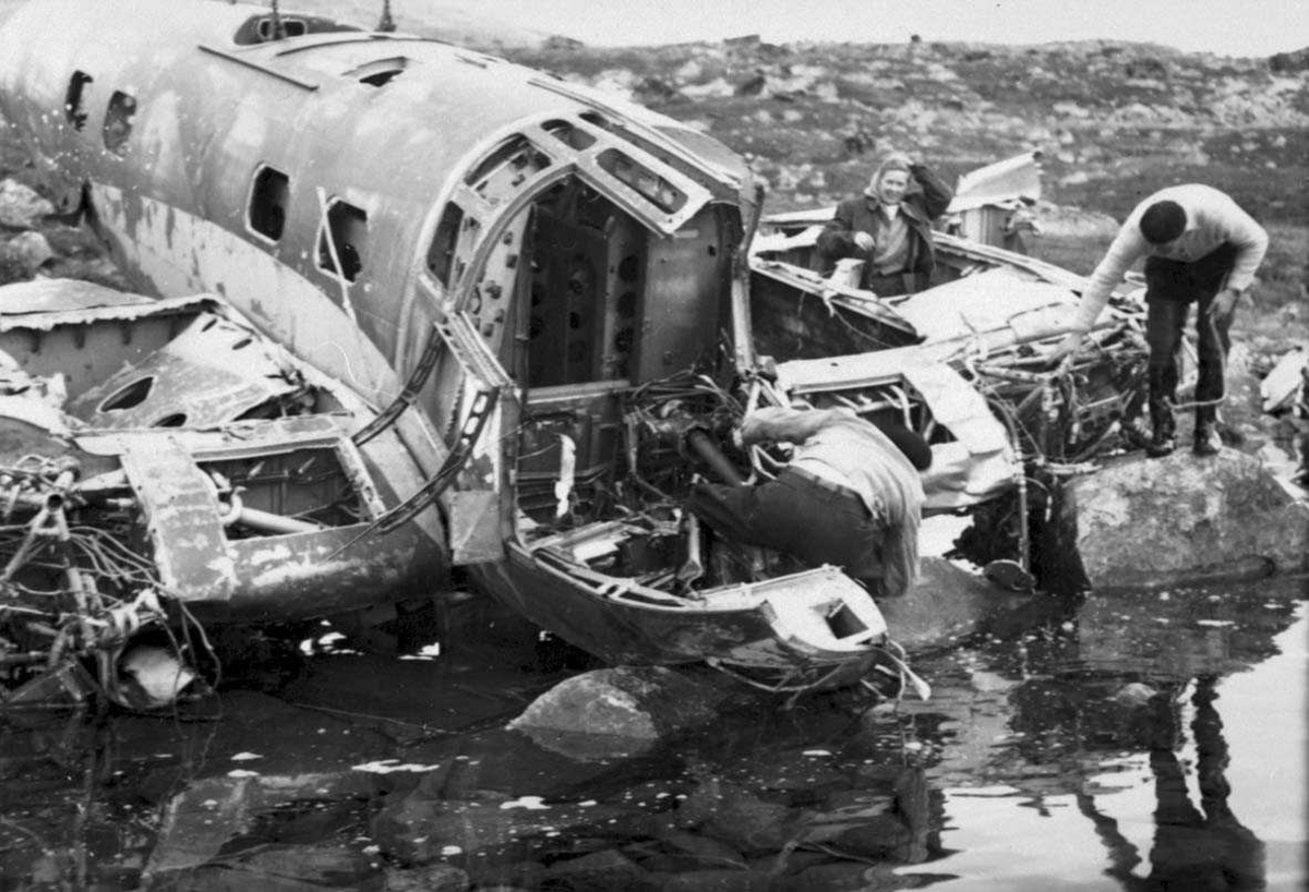 Ett flyvrak ved vannkanten, He 111H-3, 1H+DN. Tre personer, to menn og en kvinne, ved flyvraket.