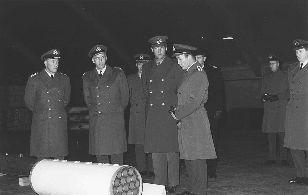 Kronprinsen og noen militære offiserer i en hangar.