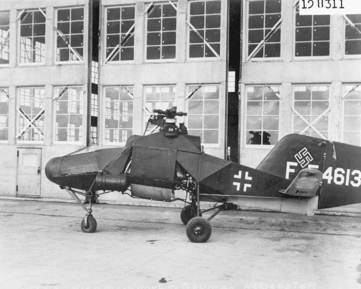1 helikopter på bakken. Flettner Fl 282 Kolibri. Står foran en hangar.