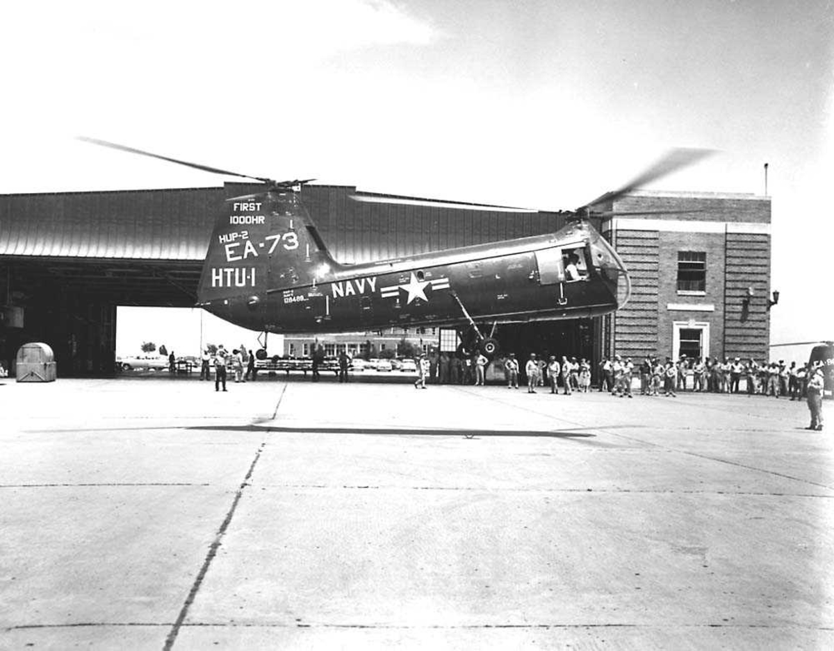 1 helikopter i luften. Piasecki HPU-2. Hangar og folkemengde i bakgrunnen.