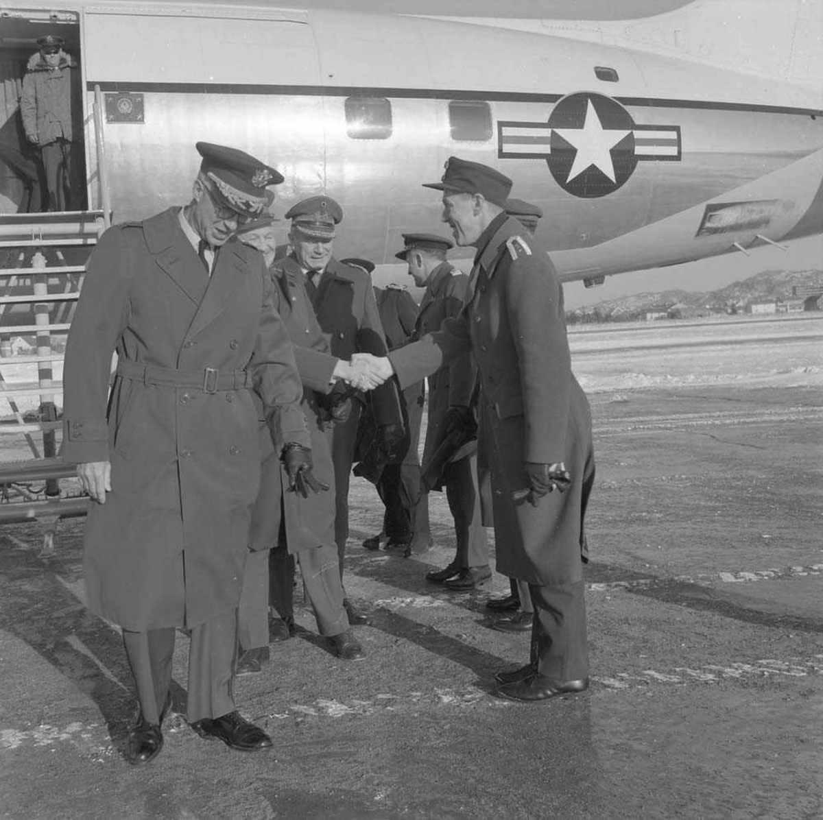 General Goodpasler besøker Bodø flystasjon. Han sees til venstre i bildet og til høyre sees Oberst E. Tjensvoll, som mottar besøket. Flyet i bakgrunnen er en Douglas DC-6.