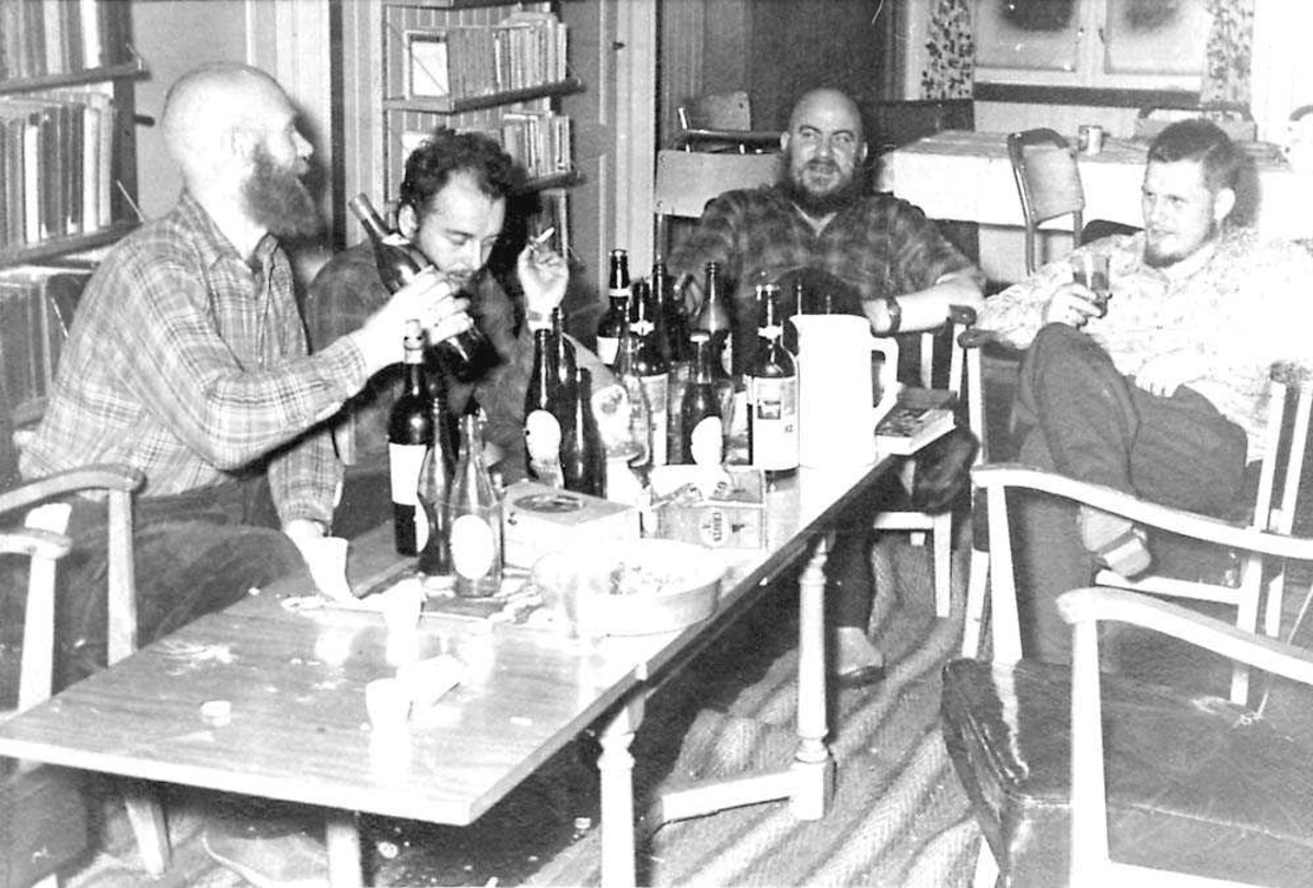 Fire personer som sitter rundt et bord og fester. Flere flasker på bordet.