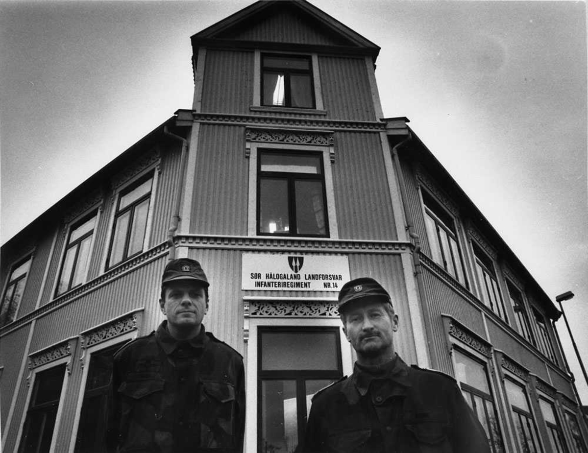 To personer som står foran en bygning, menn i militæruniform.
På bygningen står det et skilt med "Sør Hålogaland landforsvar infanteriregiment nr. 14".
