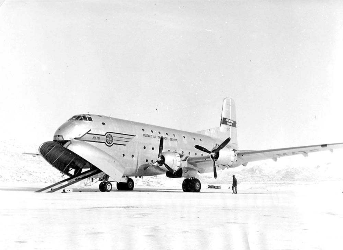 Lufthavn. Ett fly på bakken, Douglas C-124 Globemaster "MATS". En person ved flyet. Fjell i bakgrunnen. Snø på bakken.