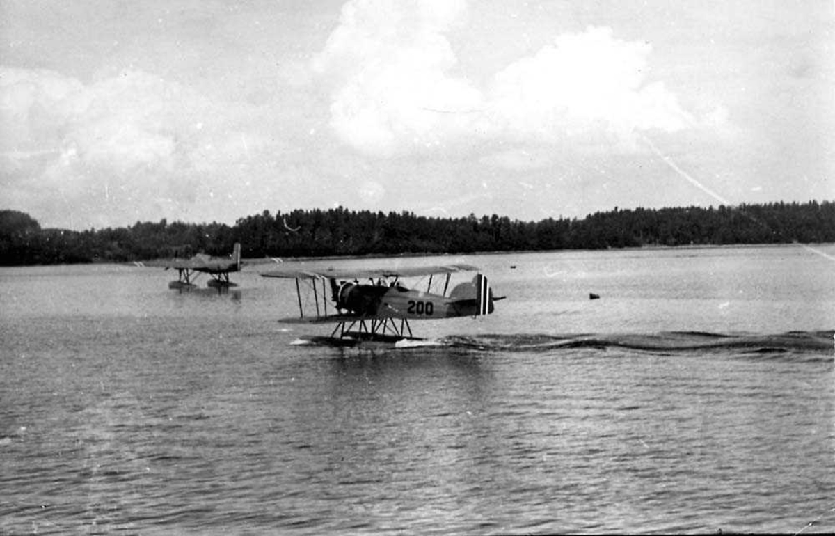 Ett fly i sakte fart på vannet, MF-10. Ett annet fly i bakgrunnen.