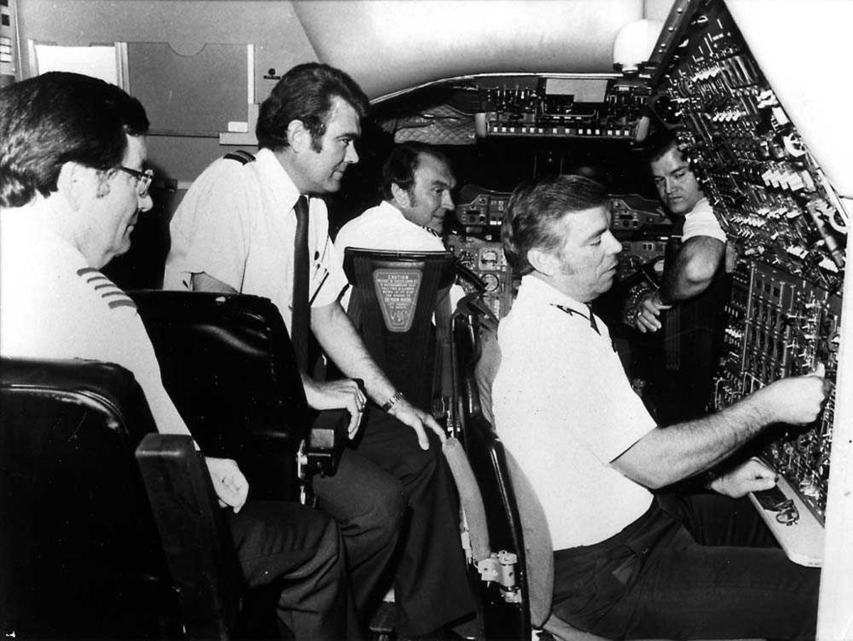 Gruppebilde. Fem personer i pilotuniform inne i cockpiten  på en Concorde-simulator.