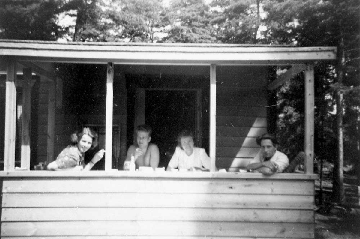 Portrett. Fire personer som sitter i ei bu/hytte og røyker.