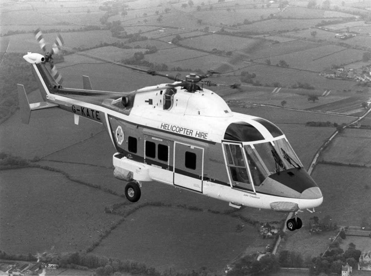 Ett helikopter i luften over dyrket mark. Westland 30-100 tilhørende Helicopter Hire Ltd, merket G-KATE
