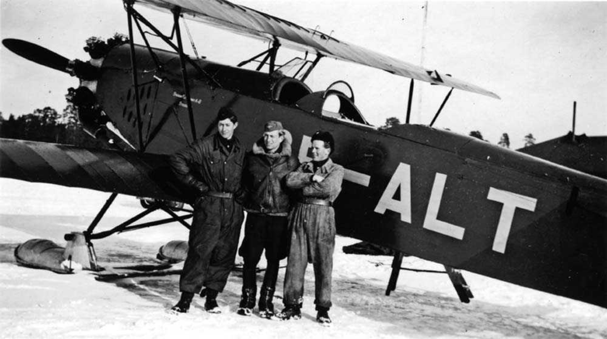 Ett fly på isen på flotører SE-ALT. Tre personer står foran flyet.