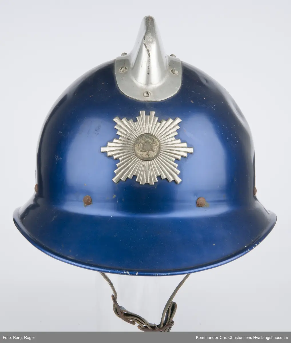 Teknikk: Fabrikkframstilt med innerhjelm av lær. Metallhjelmen er blå med blank kjøl og brannvesenets emblem i sølv
