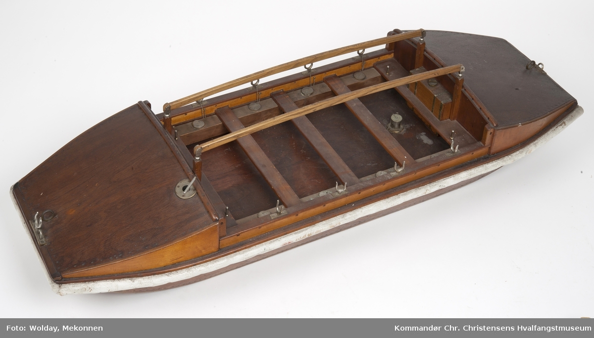 Modell av en flatbunnet båt, med 4 par årer, seil, vrikkeåre, flagg, en slags parasoll eller drivanker ?  samt davit m.m.
Et form for «landgangsfartøy» ?