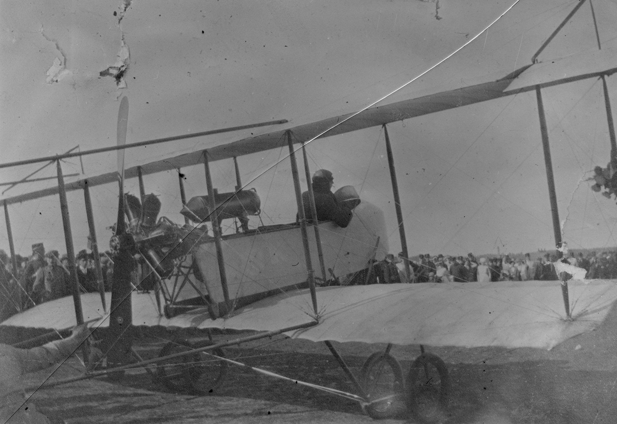 Franske flygaren Maurice Chevilliard anländer till flygfältet i Malmslätt i flygplan Farman HF 20, 1913. Folksamling i bakgrunden. Vy bakifrån.