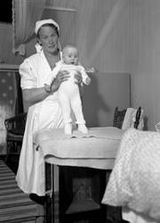 Kvinne som holder baby ved stellebord 17 April 1938
