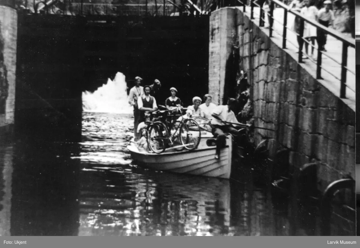 Fartøy, motorbåt, snekke.
Motorsjekte fullastet med ungdommer og en sykkel passerer under en bro.(Telemarkskanalen)