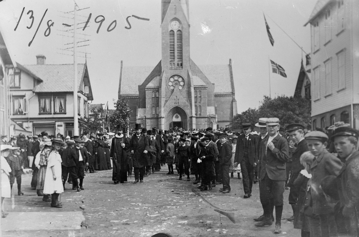 Torvet, utenfor Vår Frelsers kirke 13. august 1905, dagen for folkeavstevningen om unionen med Sverige.  Flere personer. Barn i fogrunnen til høyre.  Kirken i bakgrunnen. Trehus til venstre og høyre. Norsk flagg i bakgrunnen til høyre.