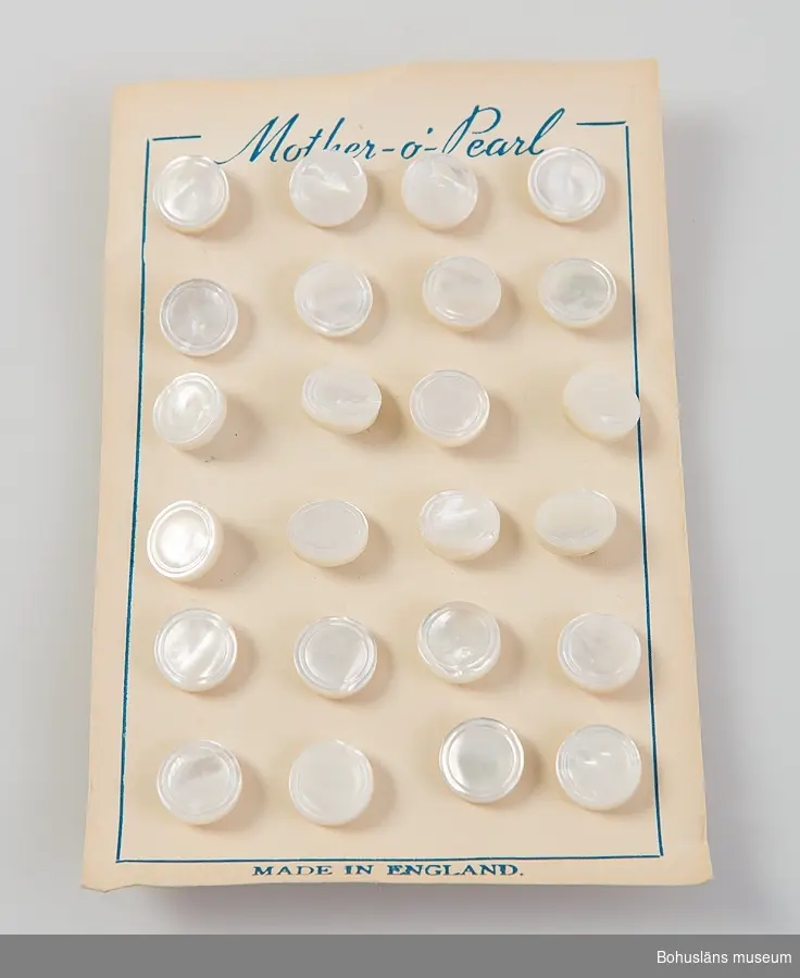 En uppsättningar med 30 fastsatta skjortknappar av vit pärlemo fastsatta mot kartongblad. På framsidan tryckt text:
Mother - o -pearl samt MADE IN ENGLAND.
Knapparna har en yttre dekorrand i relief. På baksidan ögla med rostfri klammer.
Se UM031726.