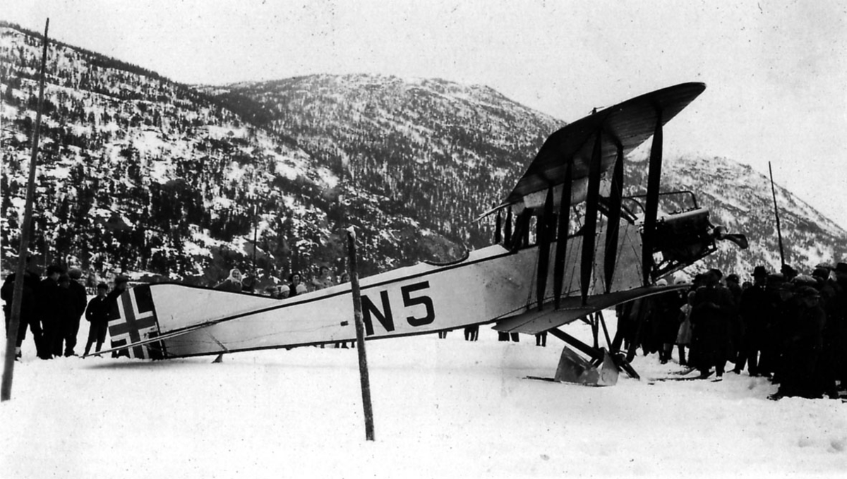 Åpen plass, flere personer ved ett fly på bakken, N5 Avro 501 A (503), med skiunderstell, snø. 