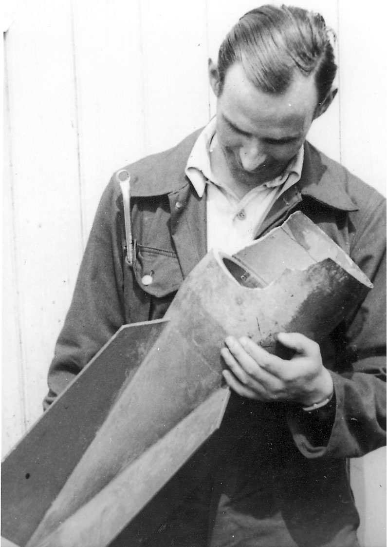 Portrett, en person, mekaniker, med noe i hendene (del til våpen/rakett for fly?)