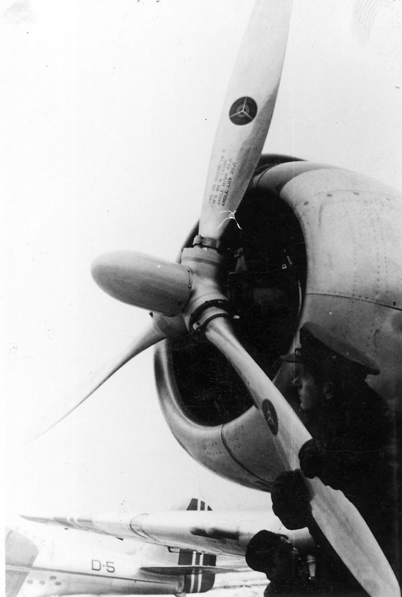 Portrett, to personer i militæruniform, ved et fly. En av dem holder i et av propellbladene. Annet fly bak, merket D-5. 