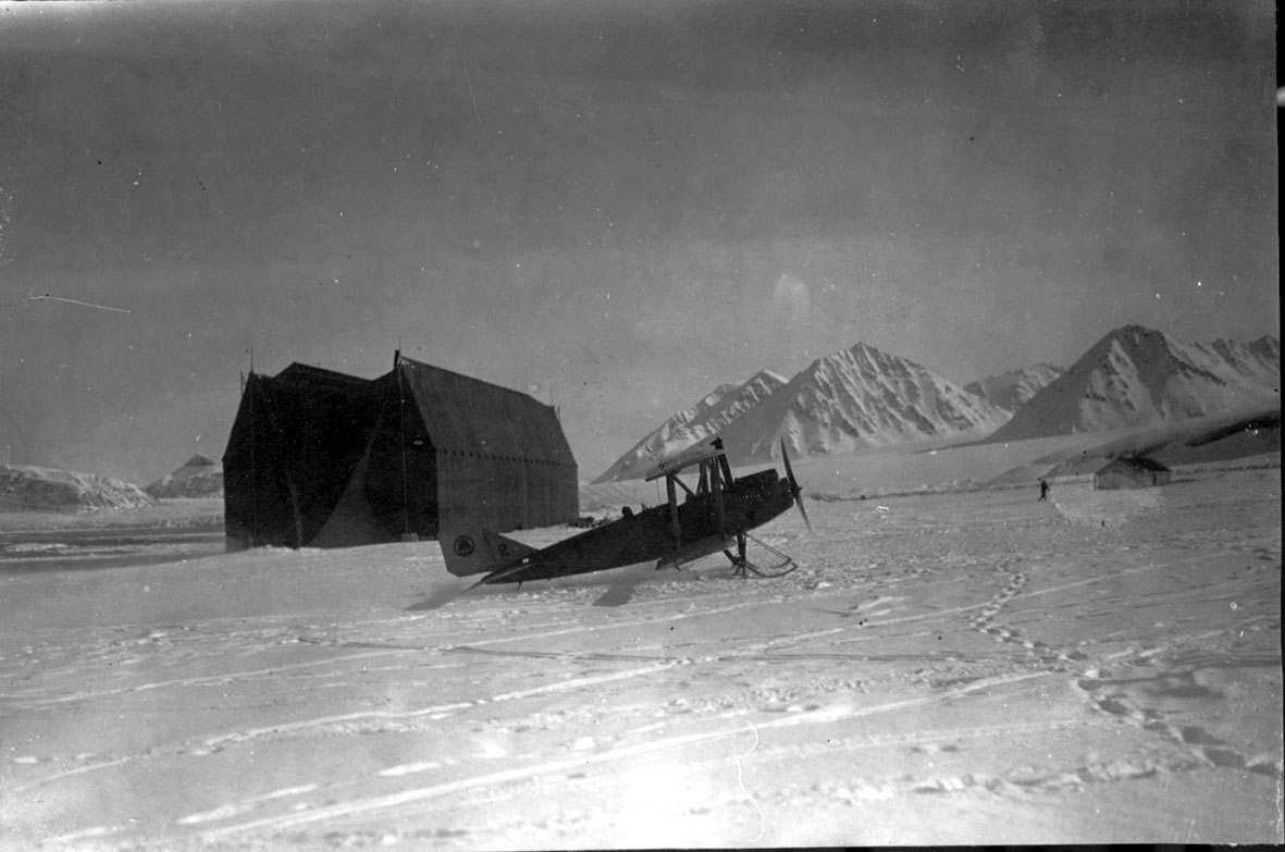 Fly, Curtiss Oriole, i forgrunnen. Luftskiphangaren bak. Snø på bakken.