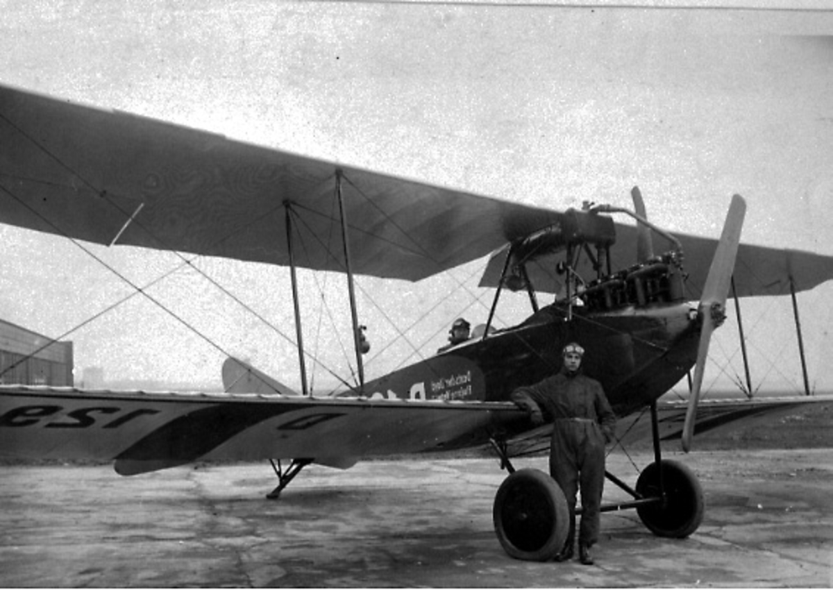 Ant. lufthavn. Fly på bakken, Albatros C.1. Skrått forfra. Person i cockpit, og en person står ved flyet, foran.