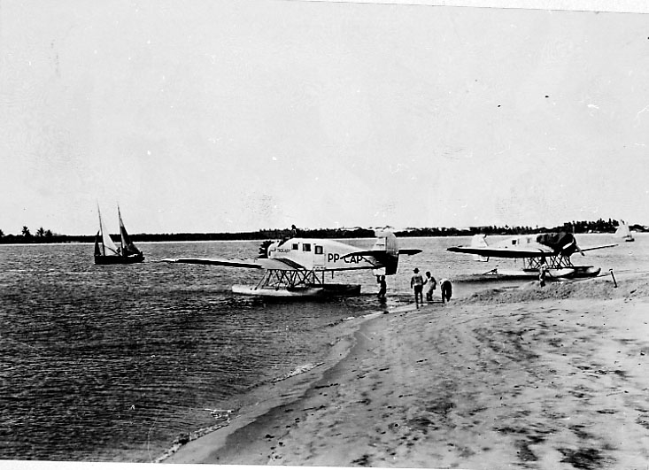 2 fly på bakken ved vannkanten. Junkers Ju-34. Flyet foran PP-CAP "Taquary., bak Ta...?. Begge fra Brazil. 1 seilbåt ute på havet.