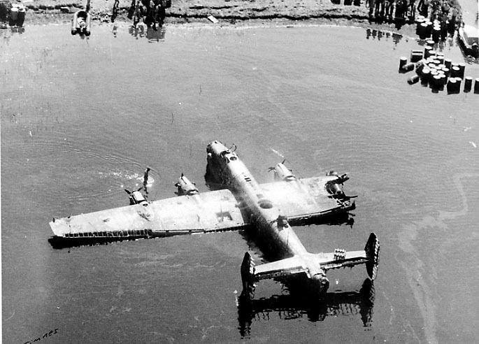 1 fly ligger skadet på bakken delvis dekket av vann, Handley Page  Halifax "S for Sugar", W.1048, fra RAF. Flere personer inne på land.