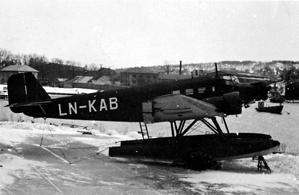 1 sjøfly står på land, Junkers JU 52 3mg 7c, LN-KAB "Tyrihans" fra DNL A/S Oslo. Bebyggelse i bakgrunnen.