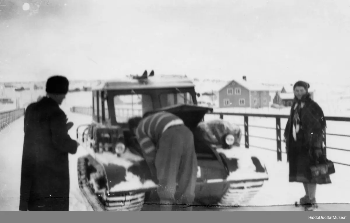 Olmmoš divvumen muohtabiilla ja guovttis vuordiba.
Mann mekker et snowmobil og to venter på at bilen skal gå.