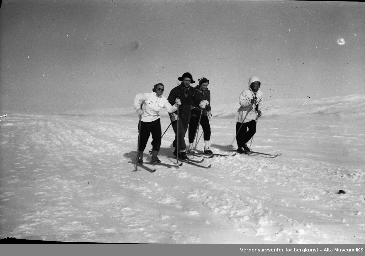 Fire mennesker på skitur, med snødekte fjell i bakgrunnen.