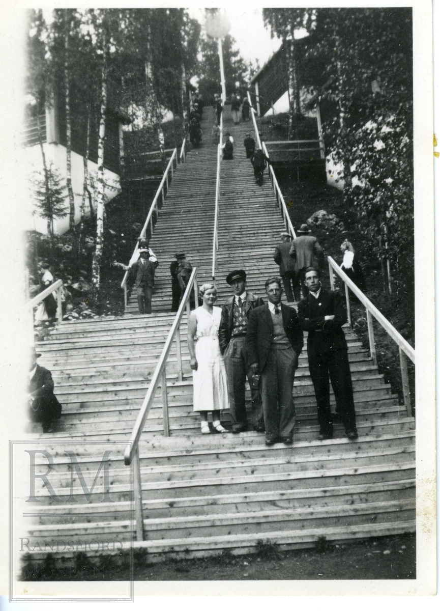 Tre menn og en kvinne ved foten av en lang trapp.