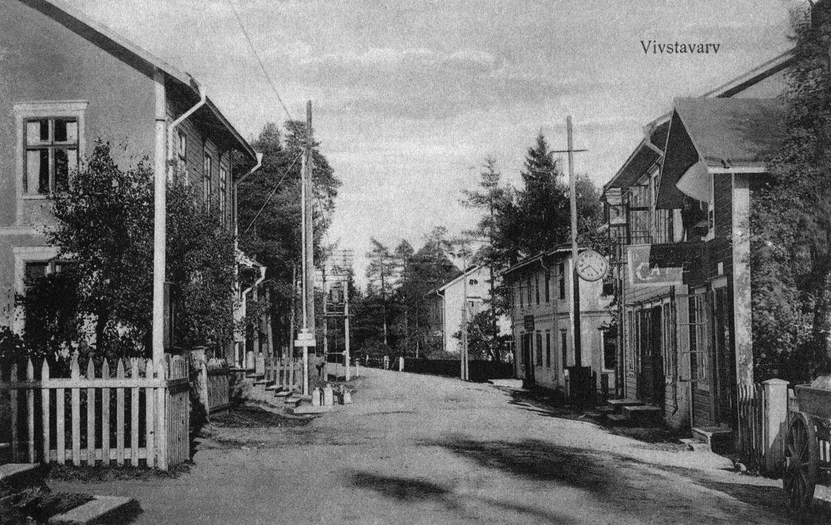 Gatuavsnitt vid Landsvägen (nu Köpmangatan) i övre Vivstavarv. Närmast till höger Caféet och urmakare Nilssons butik därefter Fröknarna Nymans mode- och sybehörsaffär. Vykort.