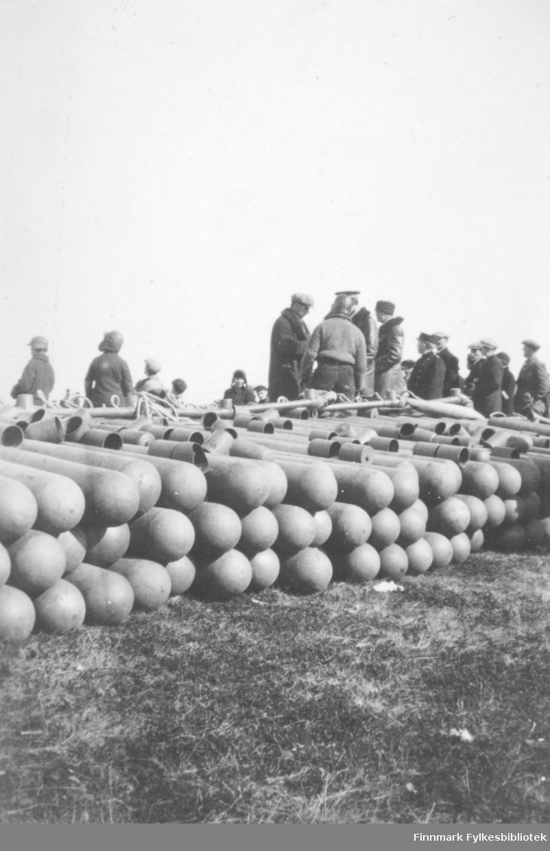 Fotografi av flere mennesker som står ved siden av  gassbeholdere som ligger på bakken. Bildet er sannsynligvis tatt i forbindelse med at luftskipet Norge var i Vadsø i mai 1926