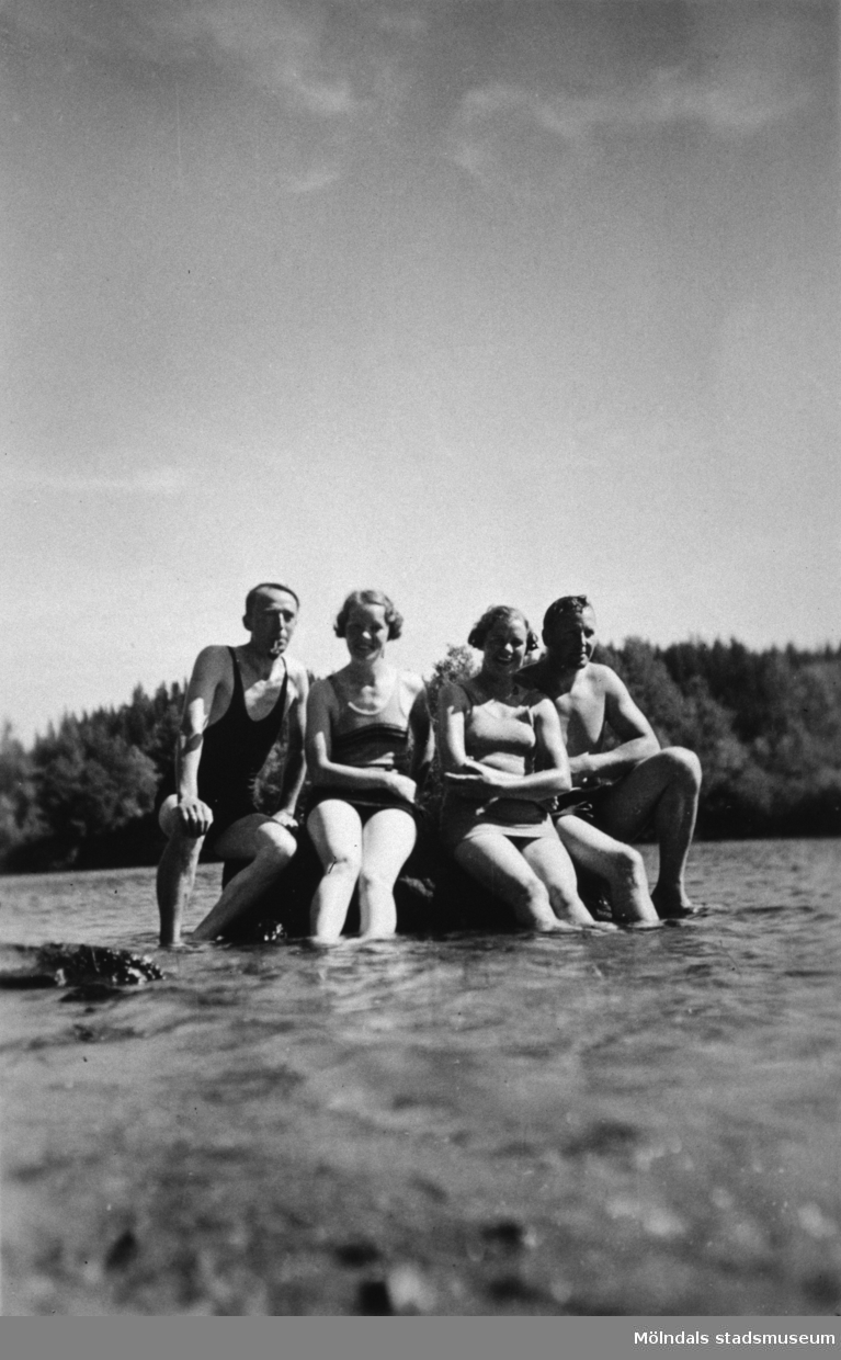 Fyra personer sitter på en sten ute i vattnet, troligtvis i Tulebosjön cirka 1930.