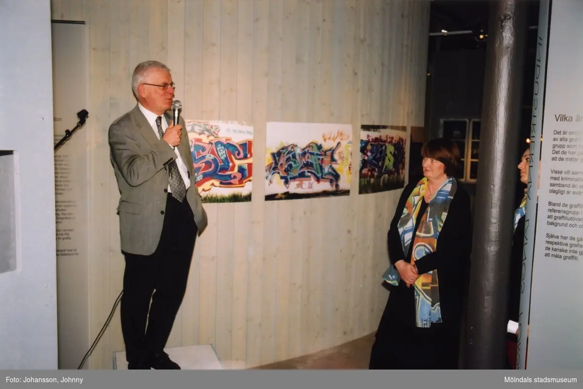 Professor Lars Nordström, ordförande i Västra Götalands Kulturnämnd, håller tal vid invigningen av utställningen "Alltså finns jag" på Mölndals museum, år 2003. Till höger ses museichef Mari-Louise Olsson.