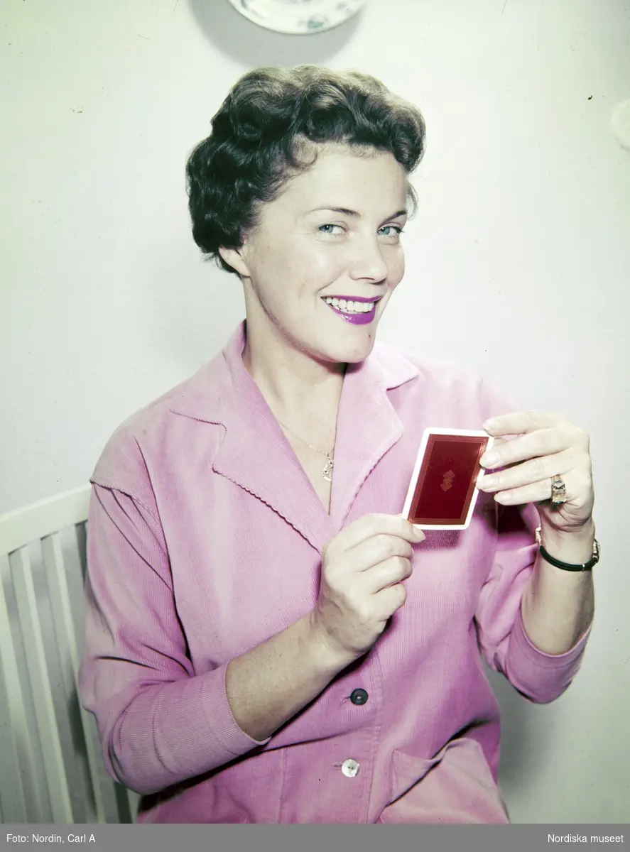 Kvinna i rosa skjorta håller upp ett spelkort.