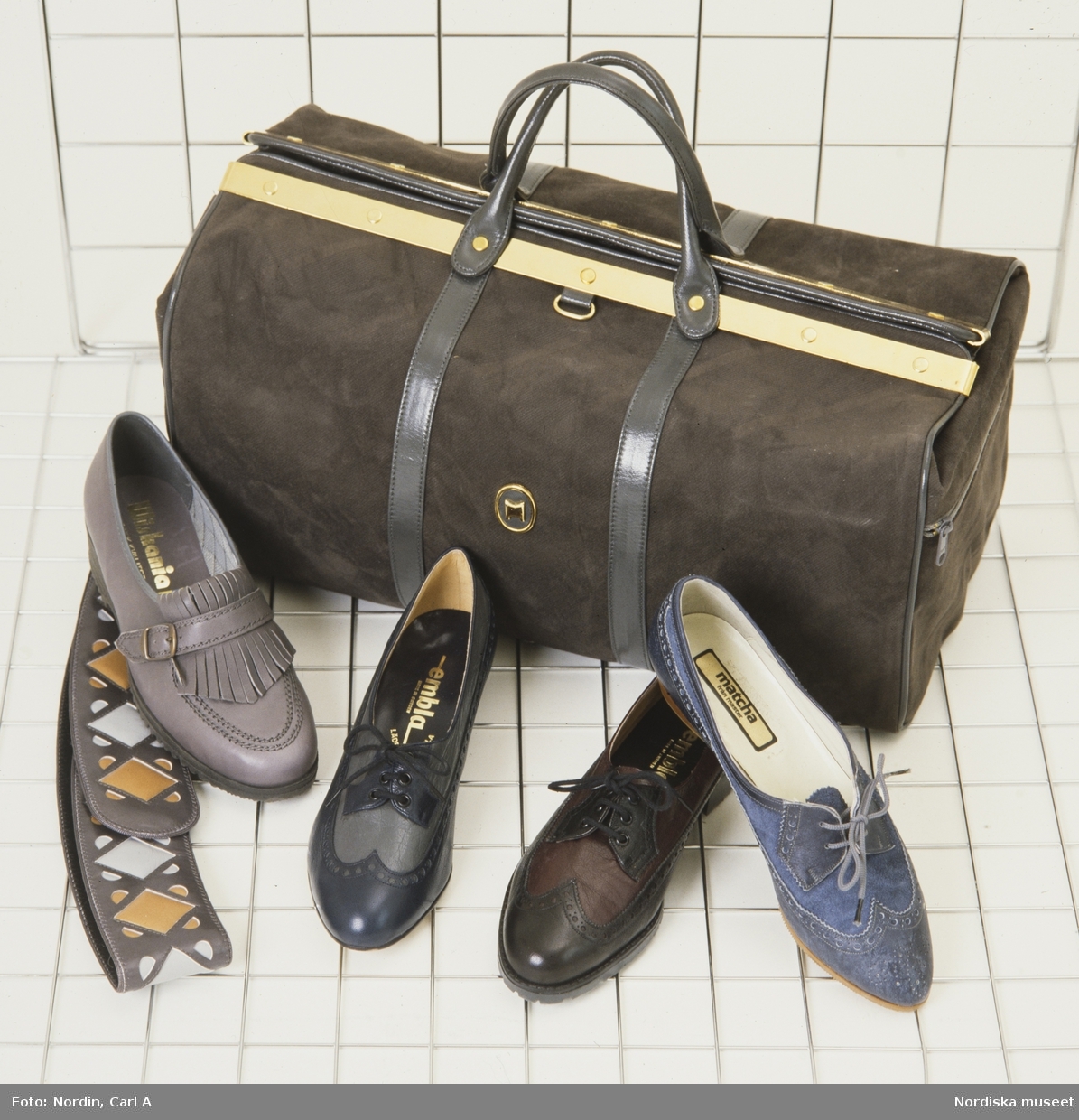 Tre snörskor i olika färger, en grå sko med fransar, ett mönstrat skärp och en brun moccaväska.