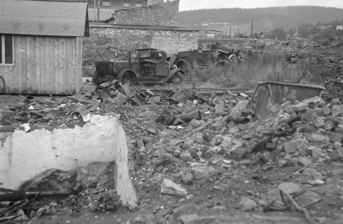 Provisorisk brakke og bilvrak i ruinene etter bombing 1940