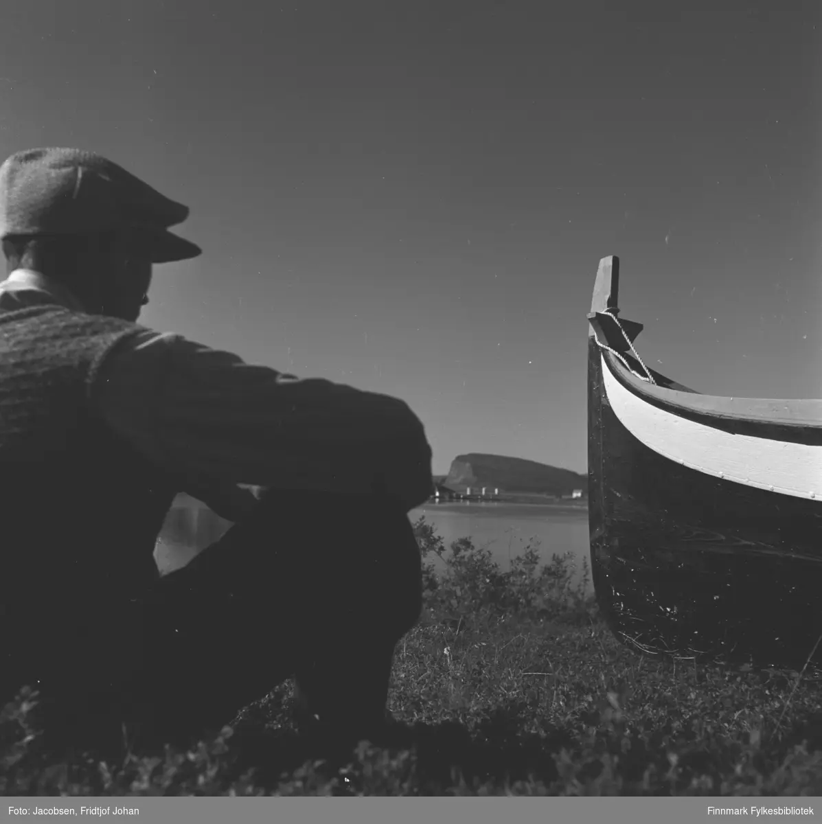 Arne Nakken ved siden av sin selvbygde Nordlandsbåt hjemme i Rypefjord. Shells tankanlegg på Rypklubbeidet og øya Håja ses mellom han og båten.