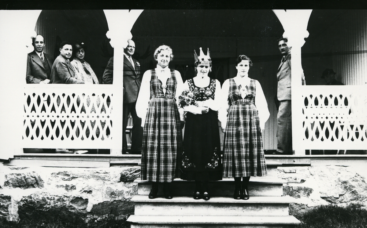 Tre kvinner i bunad på trapp foran inngangsparti, fru Lappen til venstre, menn bak. Kåring av Valdresprinsessa 