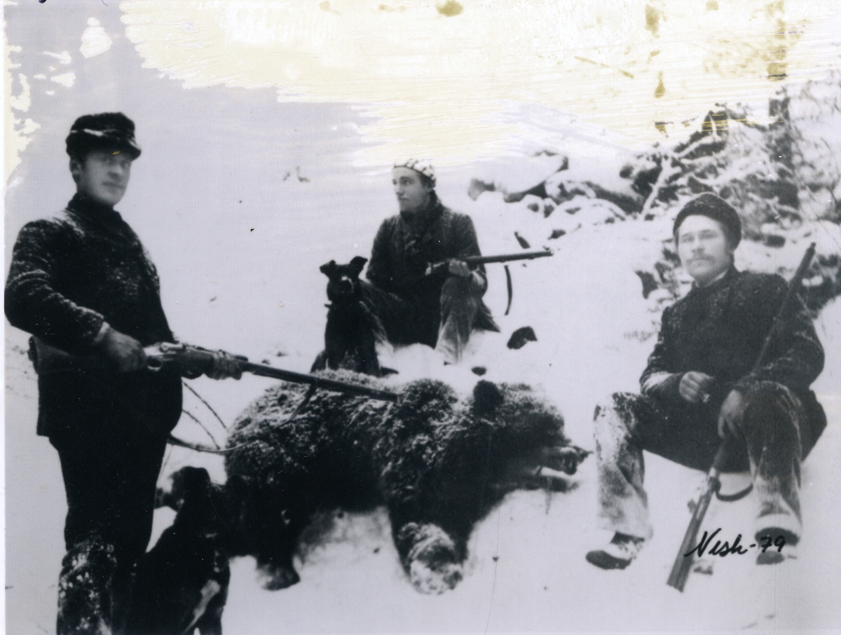 3 jegere, "Vøliskarene" (Vårum) sitter rundt ei binne de har skutt. Alle har våpen. To hunder er også med. Det er snø på bildet.
Binne ble skutt like sør for Tingvang i Øystre Slidre. Fra venstre; Knut Vårum,Torleiv Moen og fotograf Li til høyre.