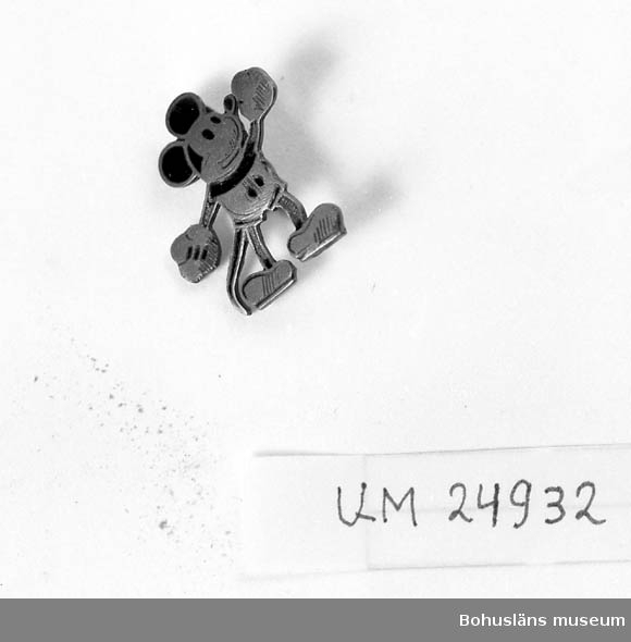 Form av en mus i kortbyxor; seriefiguren Musse Pigg. 
Svarta detaljer har delvis försvunnit från ben och armar.